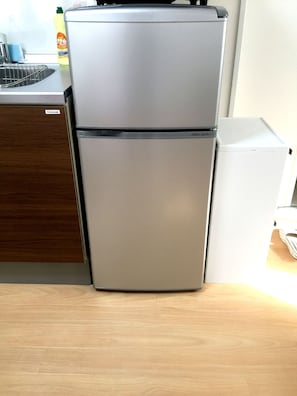 Una cocina con un refrigerador de acero inoxidable, un armario de madera y un basurero blanco.
