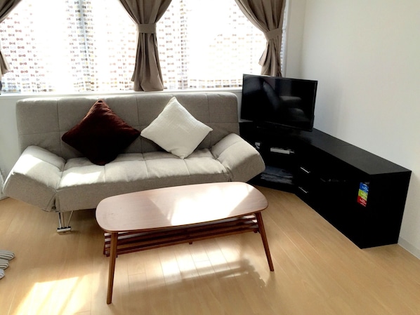 Una sala de estar moderna con un sofá gris, una mesa de centro de madera, un mueble de entretenimiento negro y un televisor.