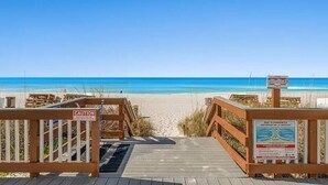 A wooden boardwalk leading to a beach with a caution sign and a poster on the right.