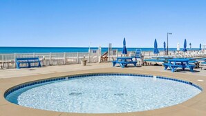 A pool area with a circular hot tub, lounge chairs, and umbrellas, overlooking a beach.