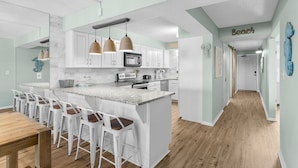 A modern kitchen with a central island, bar stools, and pendant lighting.
