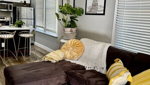 A modern living room with a sectional sofa, a dining area, and a kitchen.