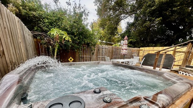 A hot tub with a control panel, surrounded by a wooden fence and outdoor furniture.