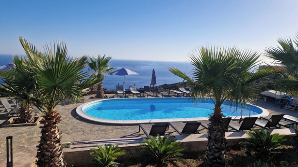 A pool with lounge chairs and umbrellas, surrounded by palm trees, with a view of the ocean. - Two-bedroom apartment with extra beds - Alba 6 (Khamma)