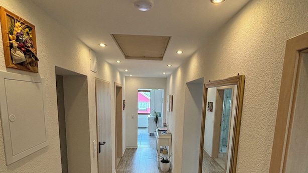 Un couloir doté d’un plancher en bois, de murs blancs et d’un grand miroir sur le côté droit.