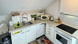 Une cuisine de taille réduite avec des meubles blancs, un lave-vaisselle, une cuisinière et un four à micro-ondes.