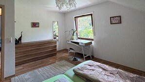 Une chambre à coucher avec un lit, un bureau et une chaise. Il y a une fenêtre qui donne sur un paysage verdoyant.