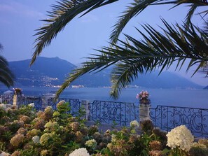 A coastal view with a metal fence, flowering plants, and a distant cityscape.