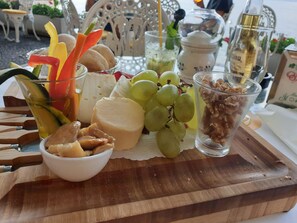 A wooden board with a variety of food items including cheese, grapes, nuts, and vegetables.