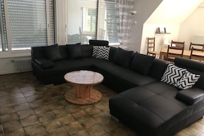 Un salon moderne avec un canapé d’angle noir, une table basse ronde en bois et un coin repas comprenant une table et des chaises.
