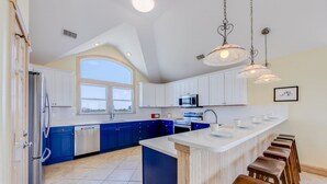 Una cucina moderna con mobili bianchi, un piano di lavoro blu e una grande isola con sgabelli.