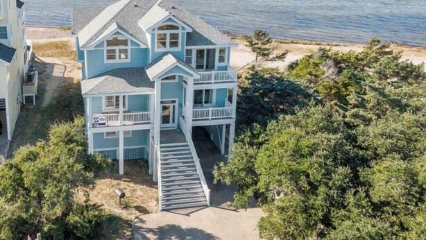 Una casa fronte spiaggia su due piani con un balcone e una scalinata che conduce all'ingresso.