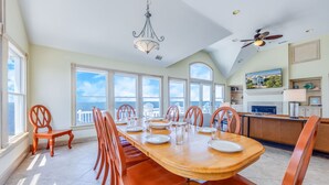 Un'ampia sala da pranzo con soffitto alto, grandi finestre vista oceano e un lampadario moderno.