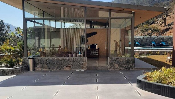 A modern building with a glass facade, a stone base, and a pool area visible in the background. - Bodhi A Boutique Hotel (Kumbhalgarh)