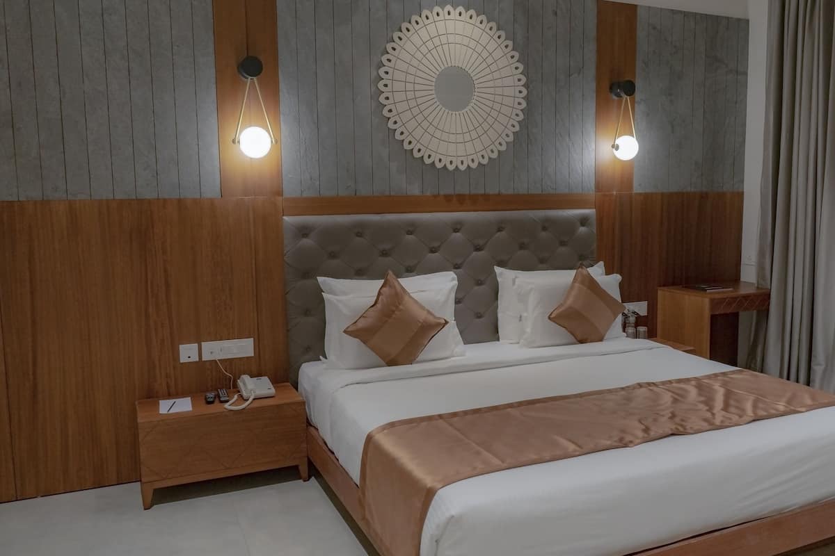 Quarto de hotel com uma cama grande, cabeceira de madeira, duas mesas de cabeceira com abajures e um objeto decorativo na parede.