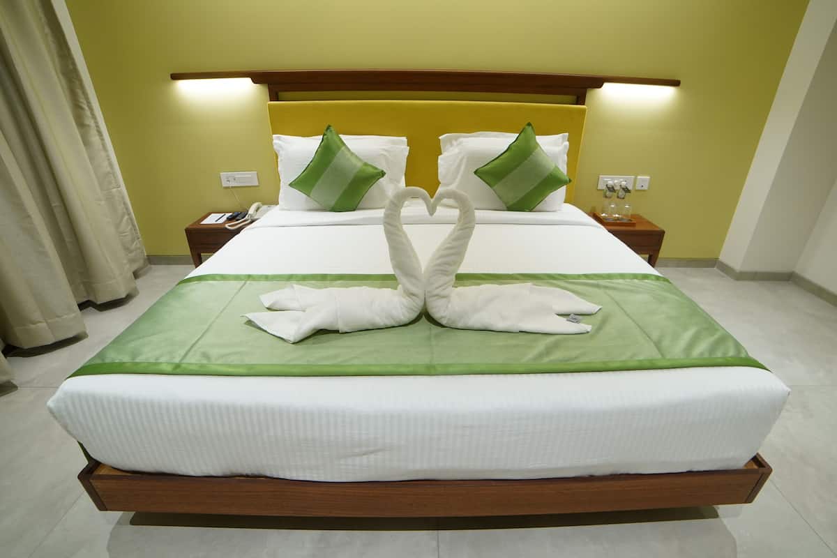 Quarto de hotel com cama bem arrumada, cabeceira de madeira e colcha verde.