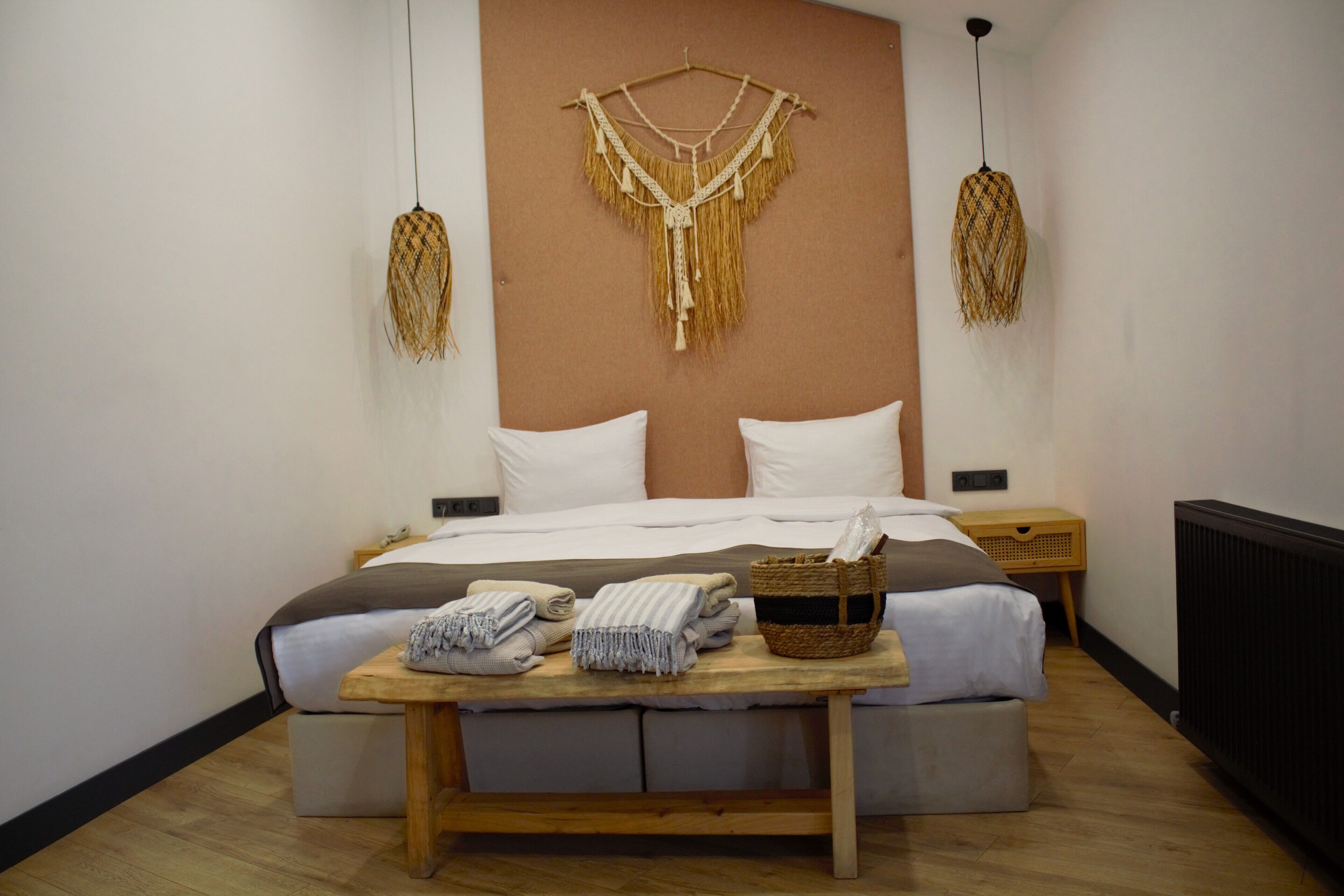 Une chambre à coucher bien rangée, avec un lit, des tables de chevet, une décoration murale en macramé et une petite table sur laquelle sont pliées des serviettes.