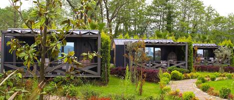 A garden with three wooden cabins, surrounded by lush greenery and a stone pathway.