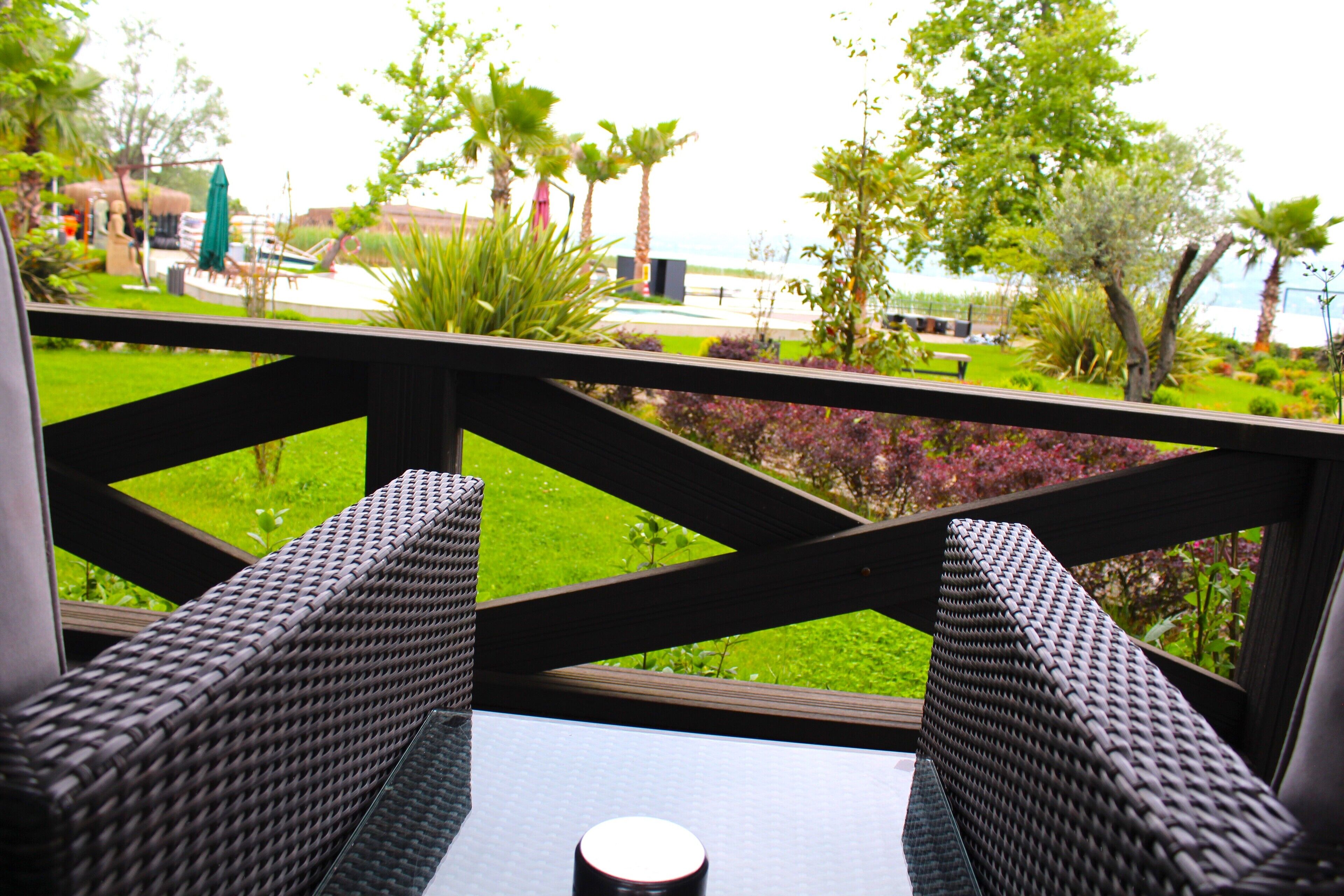 Una silla de mimbre y una mesa en un balcón con vista a un jardín y una piscina.