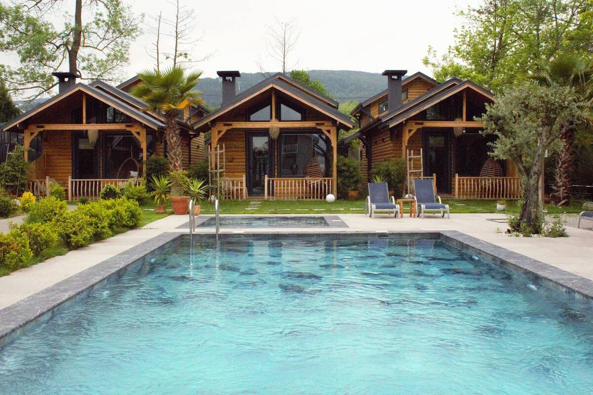 A pool area with wooden cabins, a clear pool, and a view of the mountains.