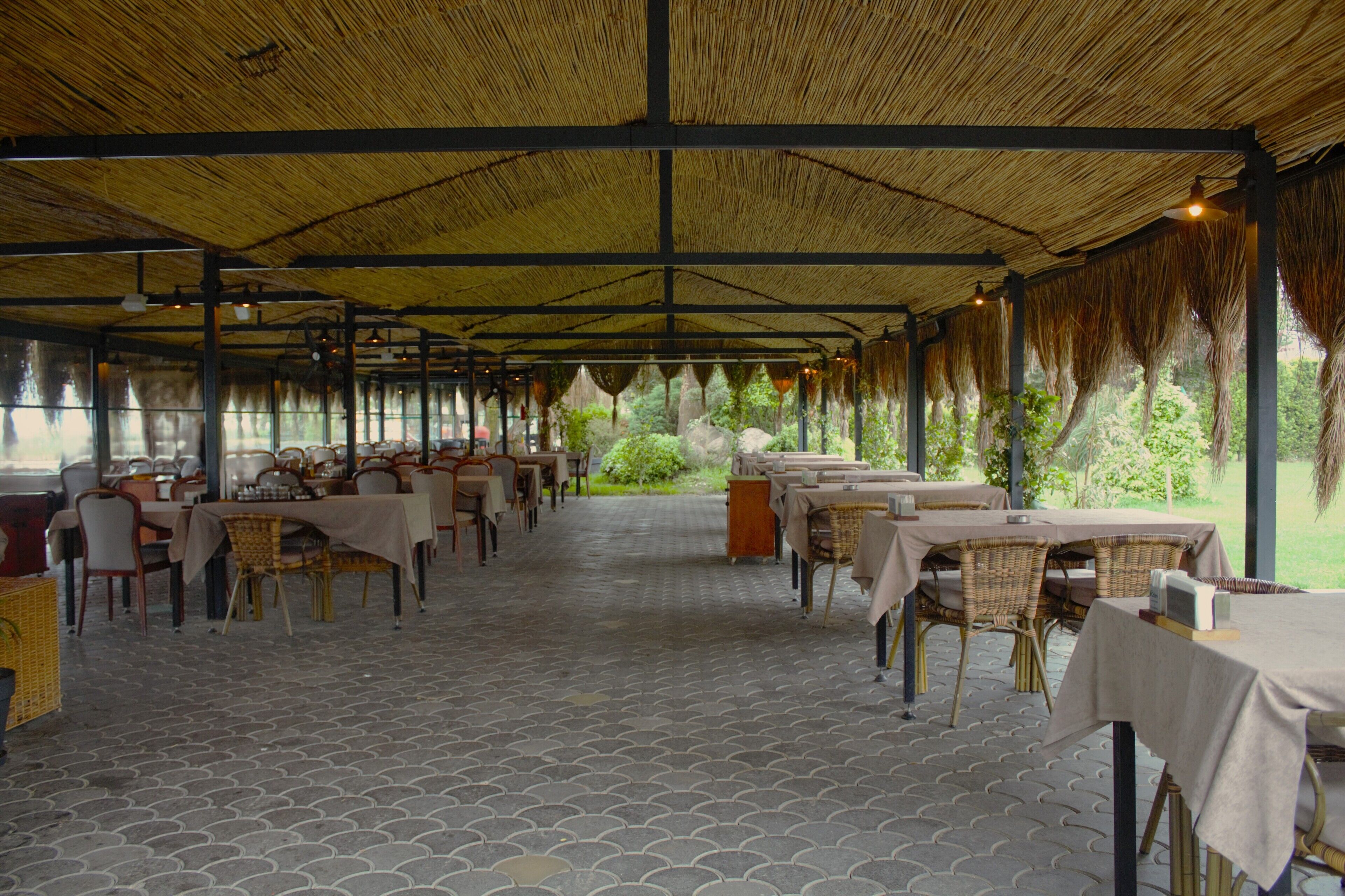An indoor dining area with tables and chairs, a patterned floor, and a thatched roof.