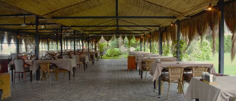 An indoor dining area with tables and chairs, a patterned floor, and a thatched roof.