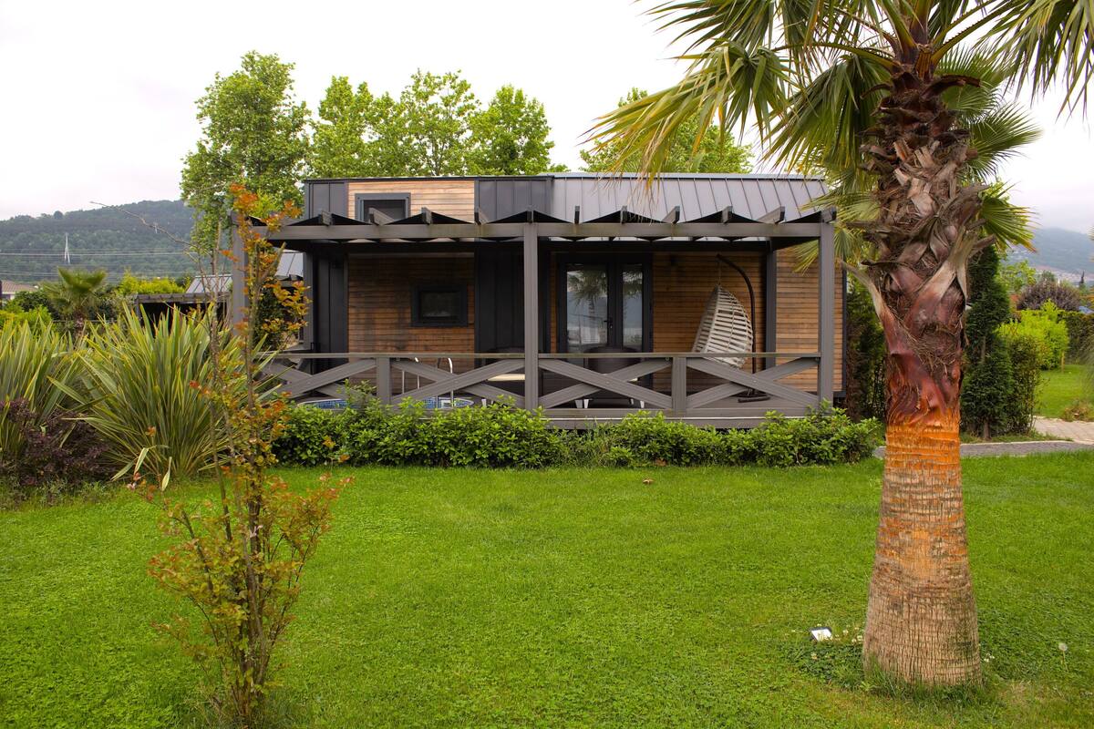 A modern house with a wooden exterior, a balcony, and a well-maintained garden with various plants.