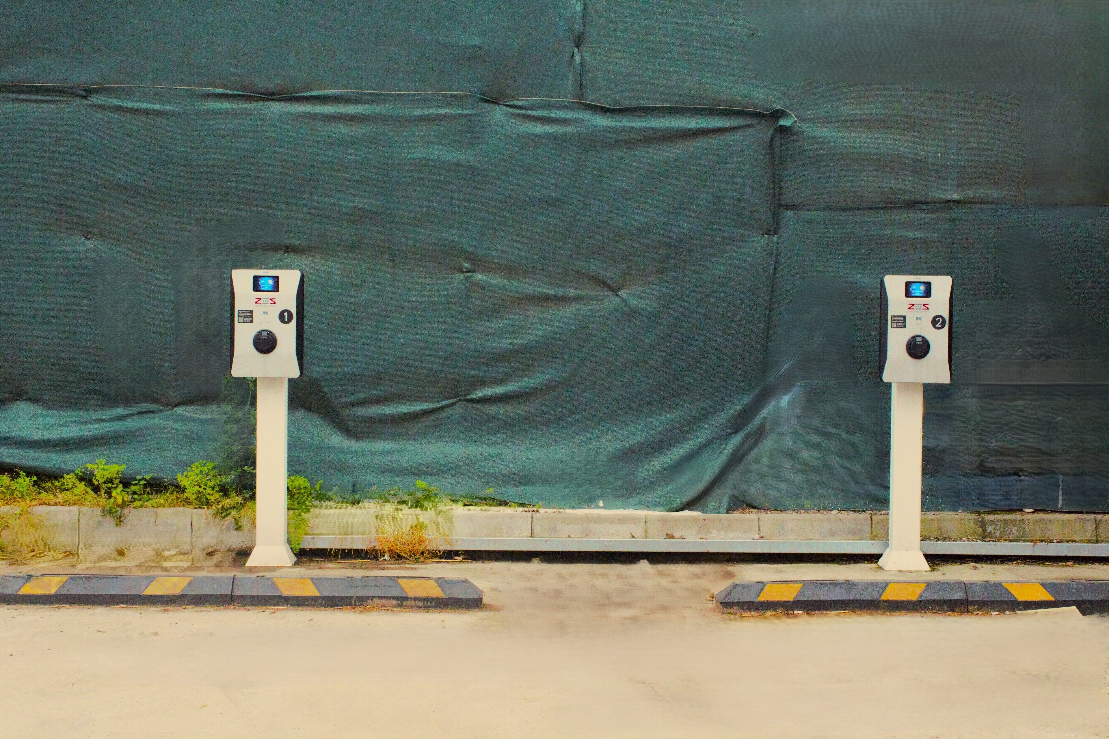 Two parking meters on a sidewalk with a green tarp in the background.