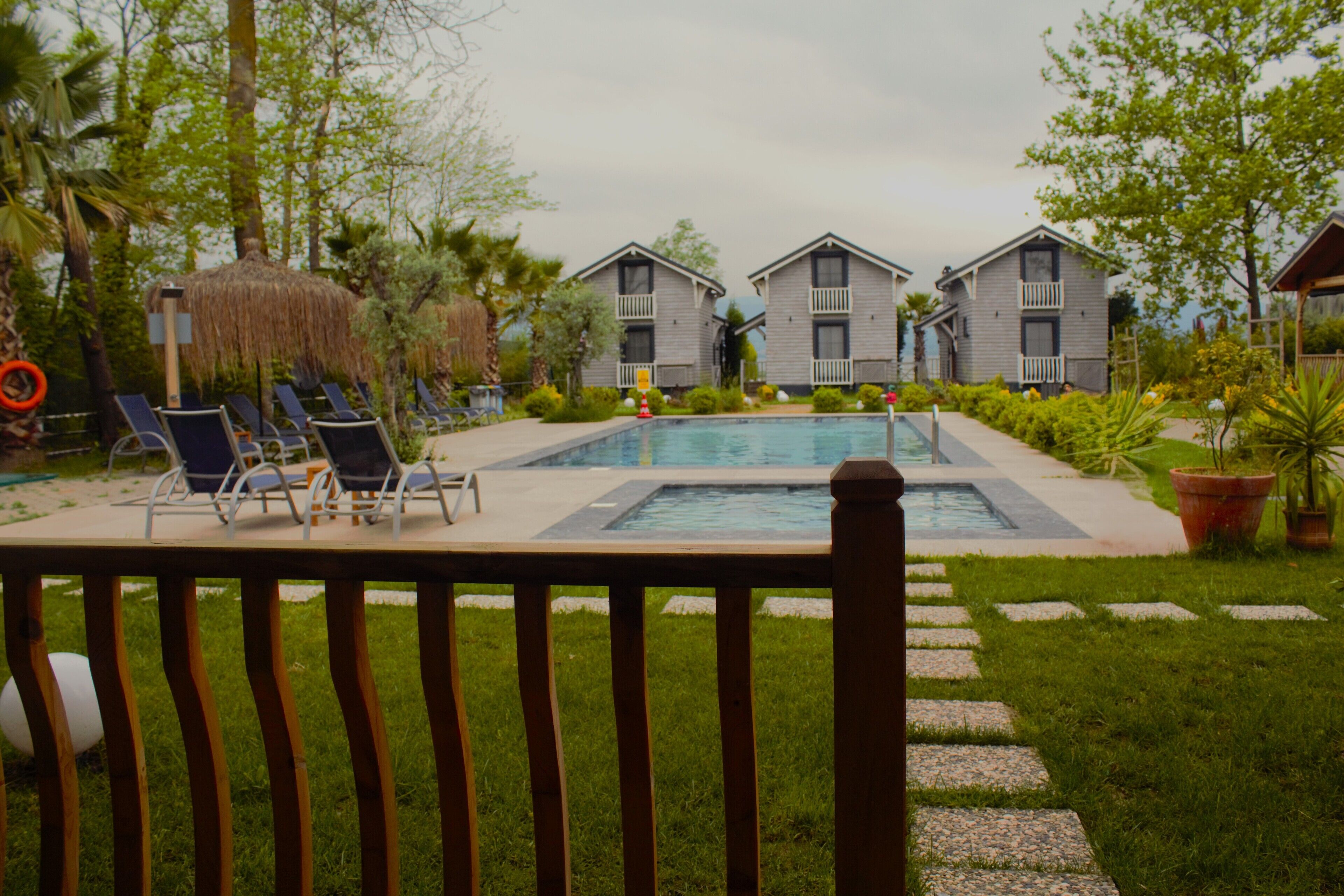 A pool area with lounge chairs, a thatched umbrella, and two-story buildings in the background.