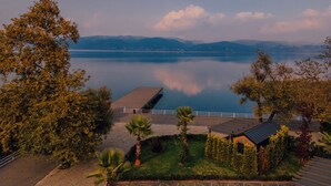 A lakeside view with a wooden deck, a small building with a sloped roof, and a distant mountain range. - Gölevi Resort Sapanca (Sapanca)