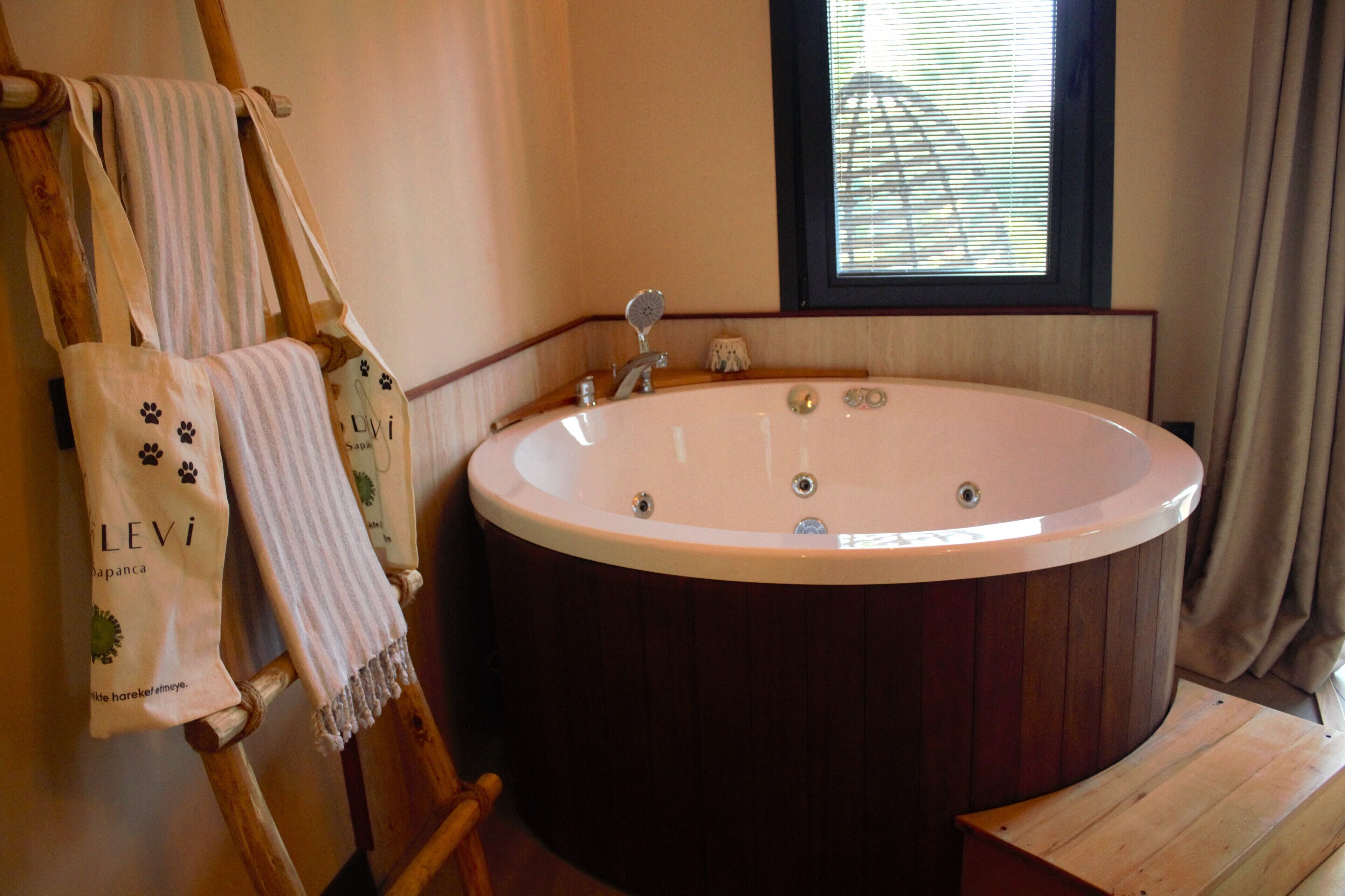 A wooden bathtub in a bathroom with a window and towels hanging on a wooden rack.