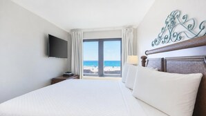 Ein Hotelzimmer mit einem großen Bett, einem Flachbildfernseher, einem Fenster mit Blick auf den Strand und einem dekorativen Metallwandbild.