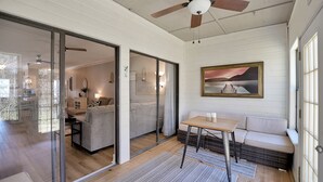 A spacious living area with a sliding glass door leading to a balcony, a ceiling fan, a painting on the wall, and a wooden table with cushions. - Upscale Escape on Lake Conroe in April Sound! “On Lake Time” 3-2 on First Floor! (Montgomery)
