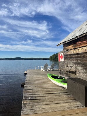 A wooden dock extending into calm water with a Canadian flag, two Adirondack chairs, and a green kayak. - Private Waterfront Family Cottage in Huntsville, Muskoka (Huntsville)