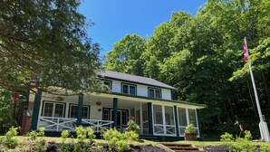 Ein zweistöckiges Haus mit Veranda, umgeben von üppiger Vegetation und einer Fahnenstange.