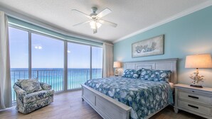 Een slaapkamer met een bed, nachtkastje, stoel en uitzicht op de oceaan.