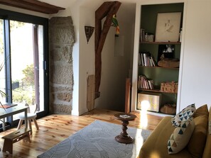 Ein gemütliches Wohnzimmer mit Holzboden, einem grünen Bücherregal, einem Holzstuhl und einer Couch mit gemusterten Kissen.