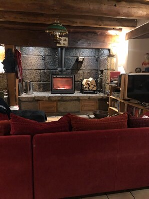 Ein gemütliches Wohnzimmer mit Kamin aus Stein, einem Fernseher und einem roten Sofa.