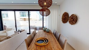 A modern dining area with a wooden table, cushioned chairs, and a large window overlooking a pool.