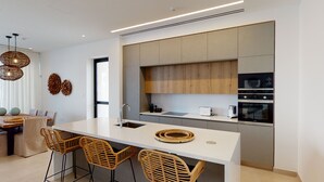 A modern kitchen with a central island, built-in appliances, and wicker chairs.