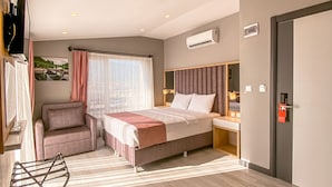 A modern hotel room with a large bed, a seating area, a flat-screen TV, and a window with curtains. - L'opera Deluxe Hotel (Edremit)