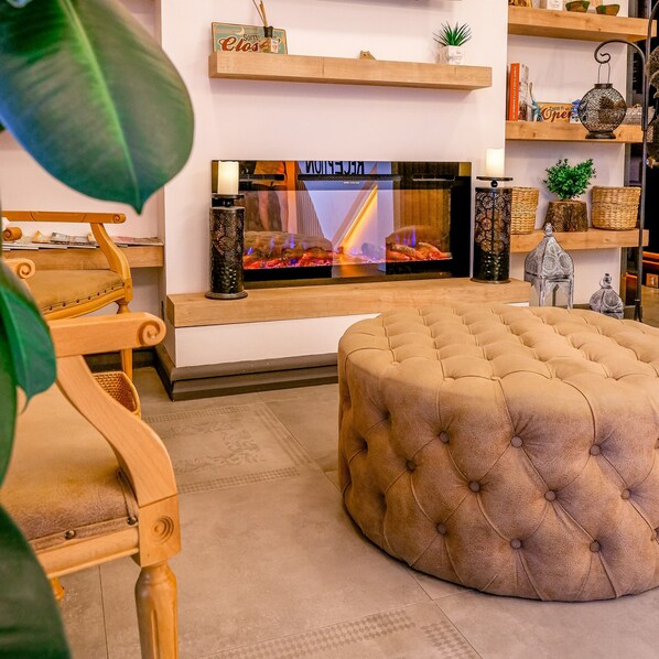 Una sala de estar acogedora con un televisor de pantalla plana grande, un otoman redondo, estanterías de madera con adornos y un sillón cómodo.