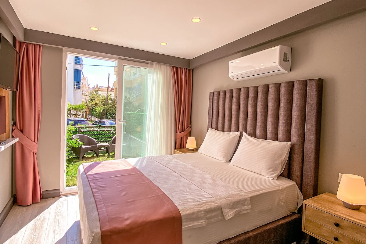 A modern bedroom with a large bed, a flat-screen TV, an air conditioning unit, and a sliding glass door to the outside.