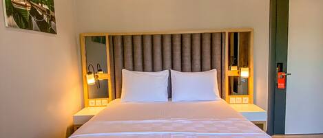 A hotel room with a large bed, a headboard with vertical slats, two bedside tables with lamps, an air conditioning unit, and a door with a red lock.