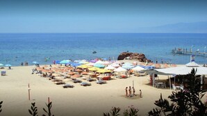 A beach with numerous colorful umbrellas and sun loungers, a rocky outcrop, and a pier extending into the water. - L'opera Deluxe Hotel (Edremit)