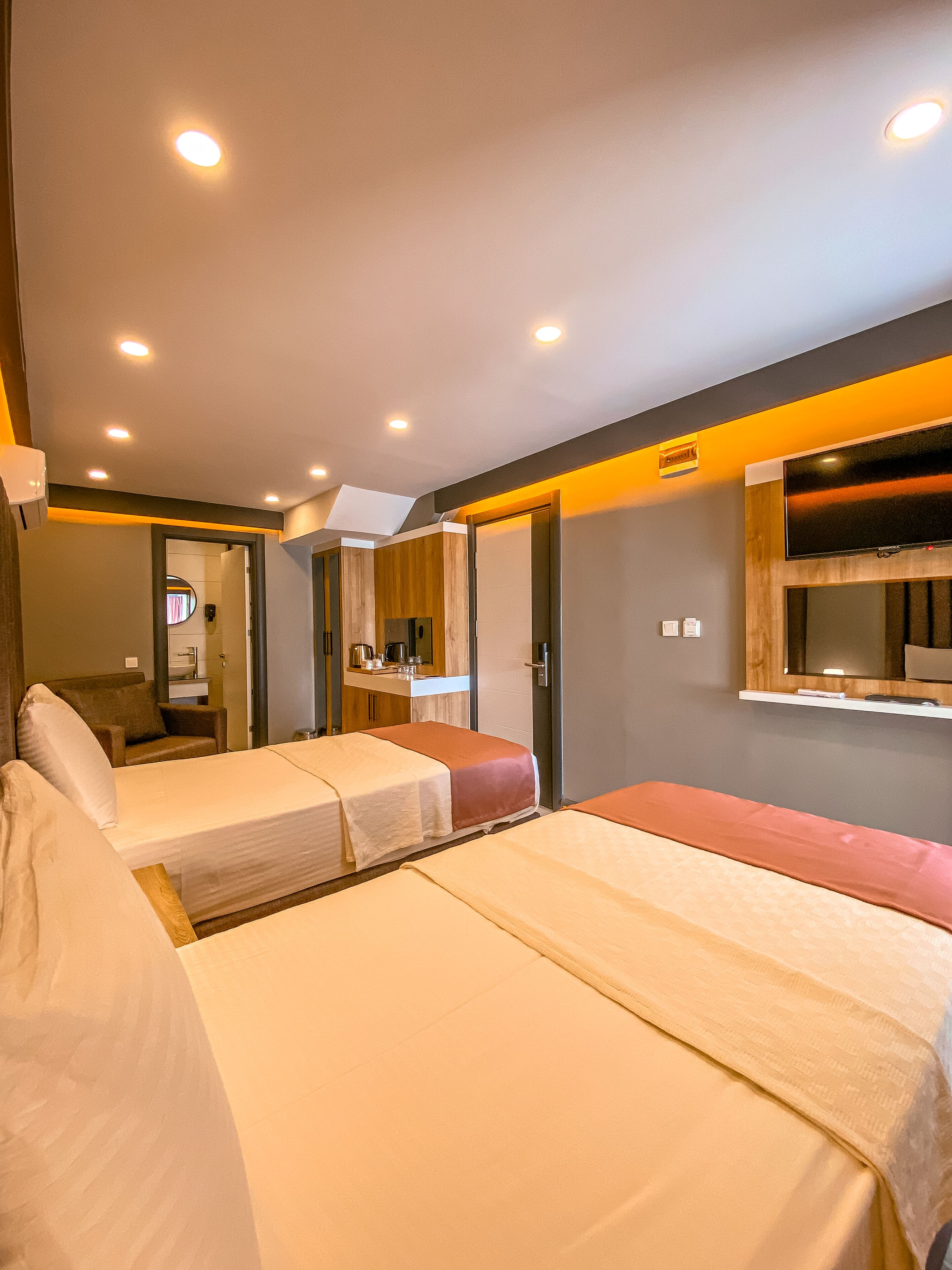 Habitación de hotel con dos camas, un espacio de descanso pequeño, un espejo, un televisor y una kitchenette.