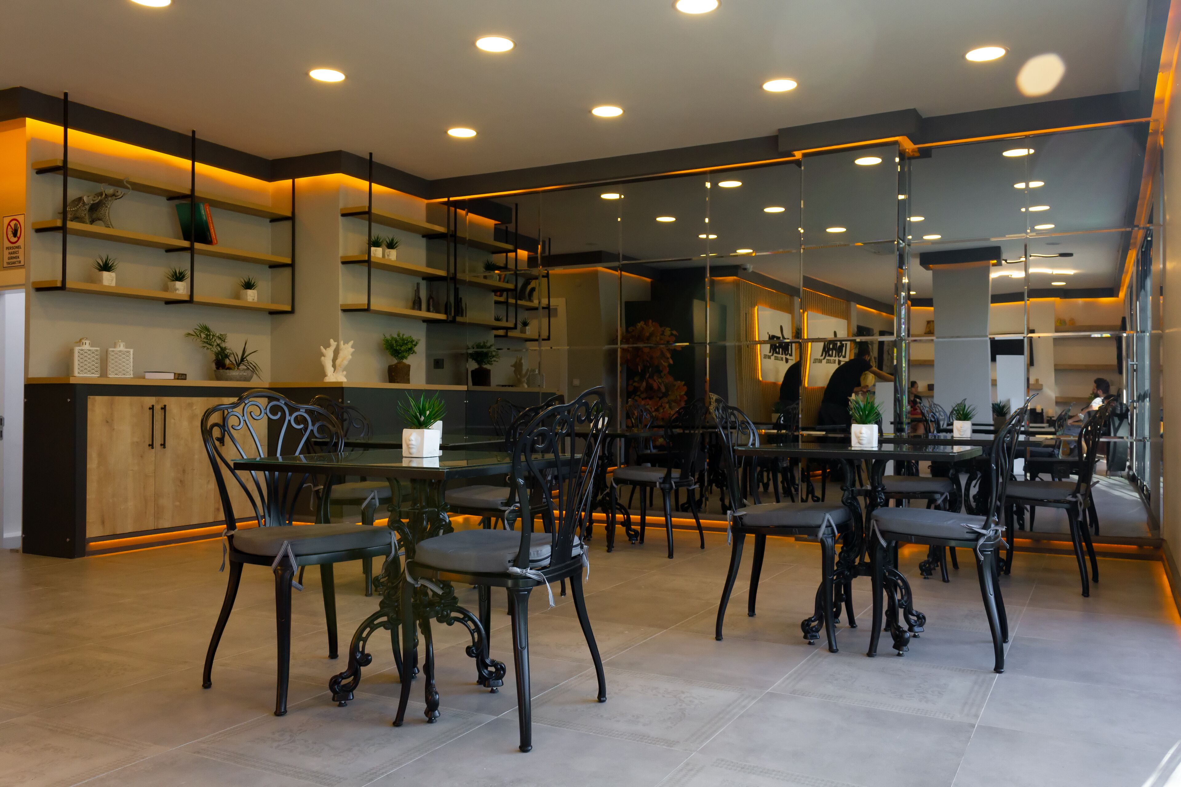 Un espace de restauration moderne avec des chaises noires, des tables en bois et des étagères ornées de plantes.