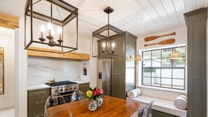 A kitchen with a wooden table, a stove, and a refrigerator. There is a window with a view of the outside. - Le Hibou Blanc (A) - Fairhope: Laid-back Sophistication (Fairhope)