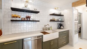 A modern kitchen with white tiled backsplash, stainless steel appliances, and wooden shelves. - Le Hibou Blanc (A) - Fairhope: Laid-back Sophistication (Fairhope)