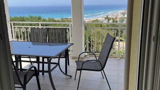 A balcony with a table and chairs, offering a view of the ocean and a coastal town.